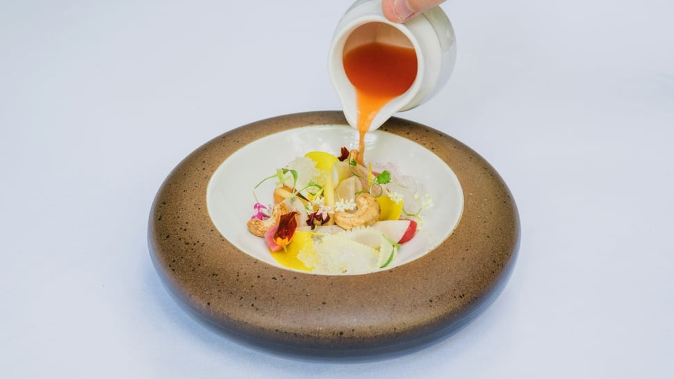 Fine dining dish with vibrant ingredients and sauce being poured, representing high-end culinary artistry